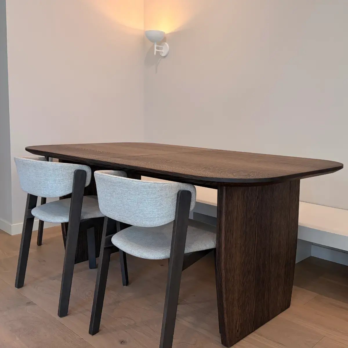 Custom extending dining table in solid rift sawn red oak with rounded corners and twin panel pedestal bases, paired with a built-in banquette bench in a Calgary dining nook