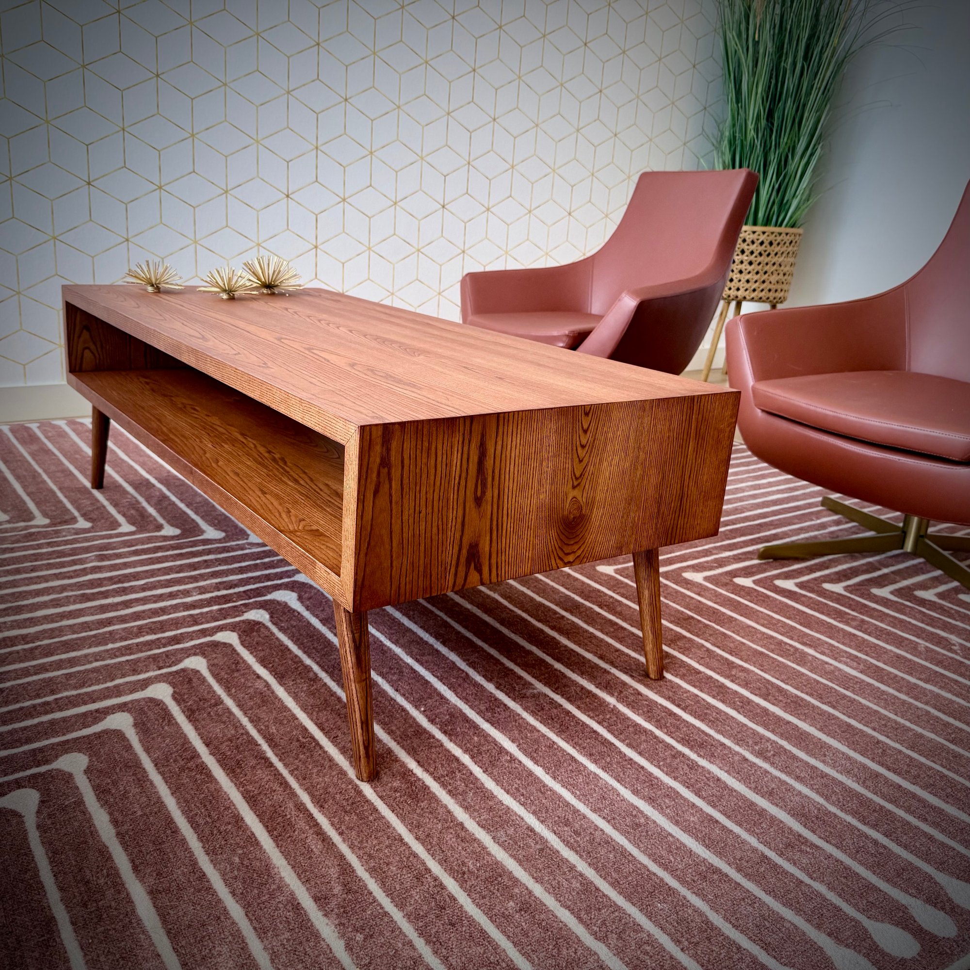 Custom mid-century modern table with prominent wood grain and tapered legs, built to complement existing leather chairs and geometric carpet in professional office space