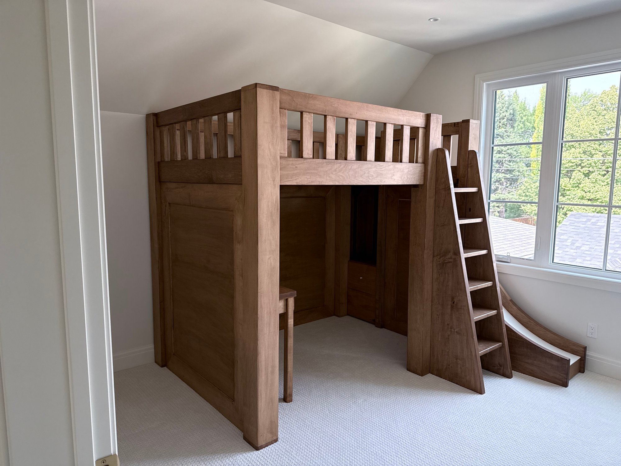 Custom solid maple loft bed with integrated slide, built-in desk and storage stairs, built for a boys' bedroom in Calgary